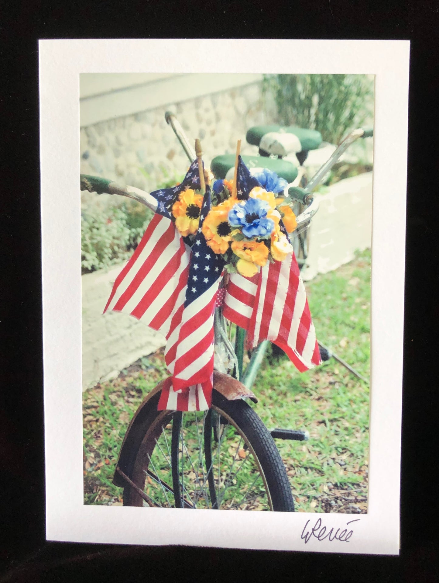 A bicycle built for two with three flags and flowers in the basket.  Faded colors in photo.