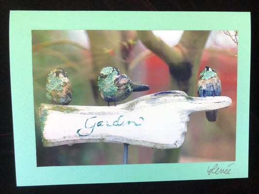Wooden garden sign featuring finger pointing and three chickadees covered with lichens.