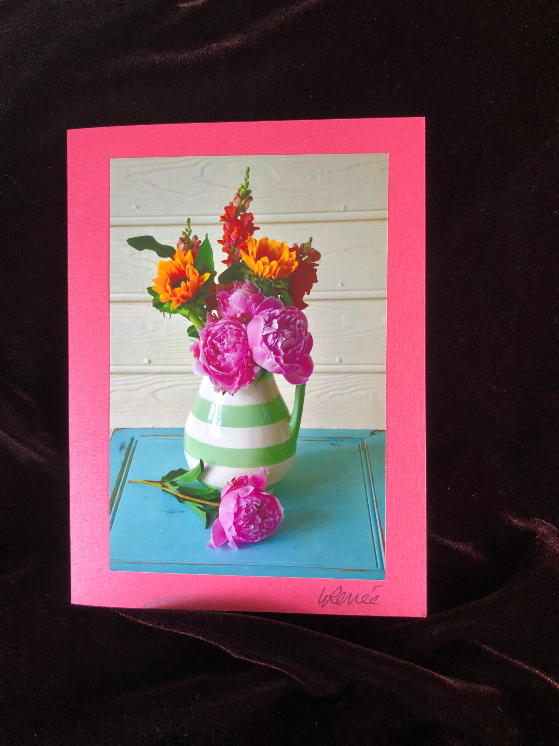 Bouquet of peonies, snapdragons, and sunflowers in a white and green striped vase.